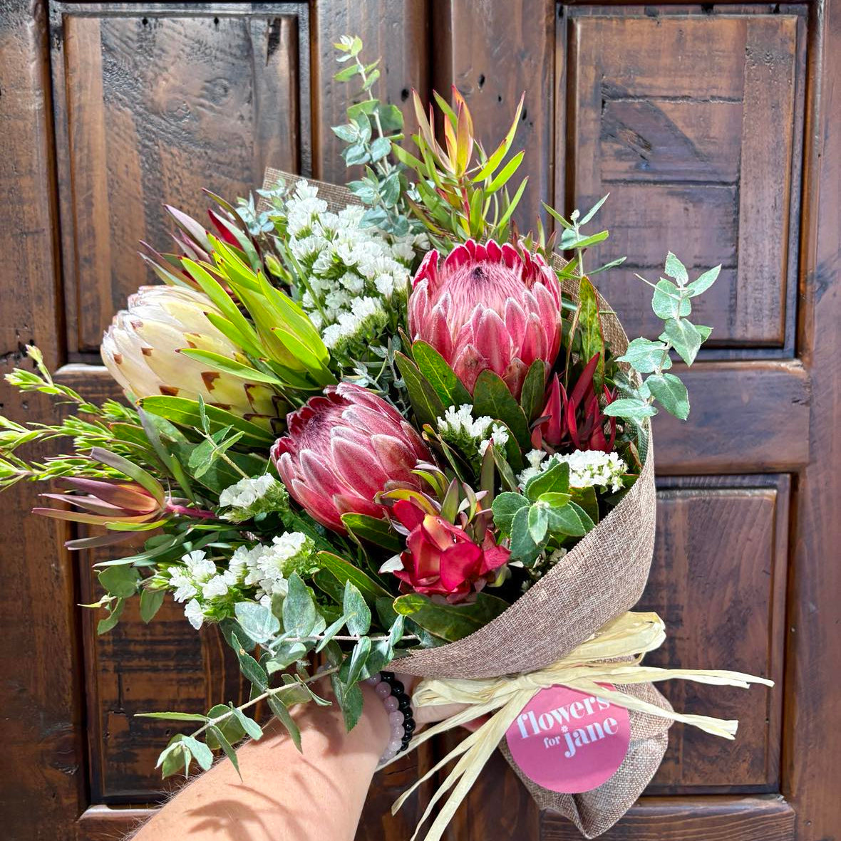Bouquet of flowers held in front of a wooden door with a visible brand tag.