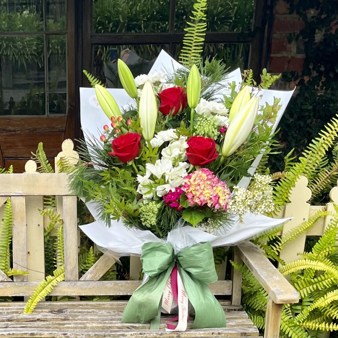 
                  
                    Bouquet of flowers with red, white, and pink flowers on a wooden bench outdoors.
                  
                