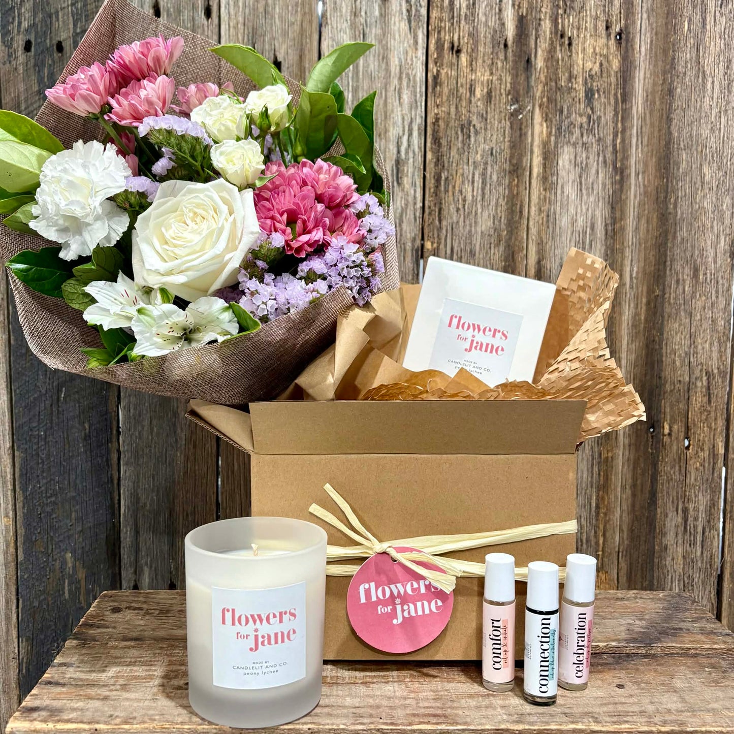 Floral arrangement, candle, and small bottles on a wooden surface with 'Flowers for Jane' branding.