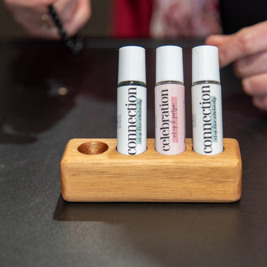 
                  
                    Three lip balm tubes in a wooden holder on a dark surface with hands in the background.
                  
                
