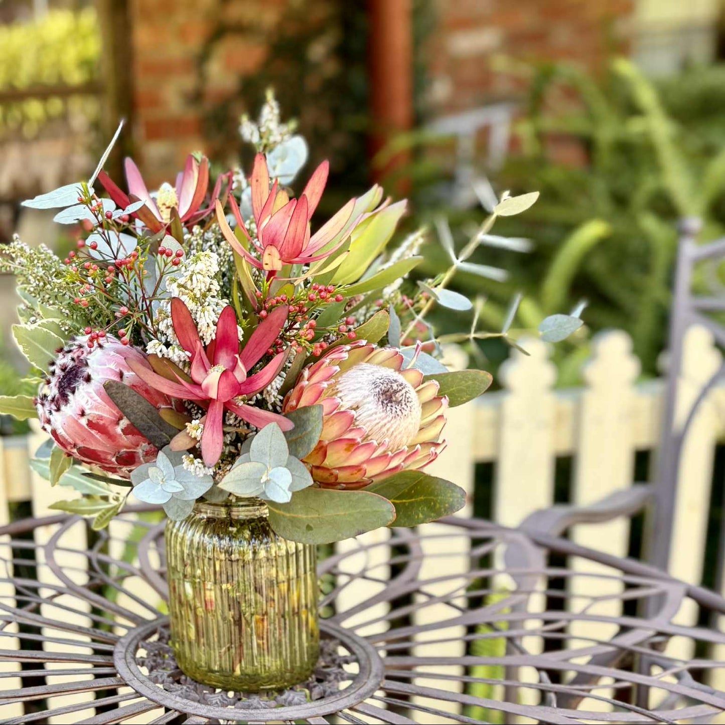 Floral arrangement in a green vase on a table with a brick wall background