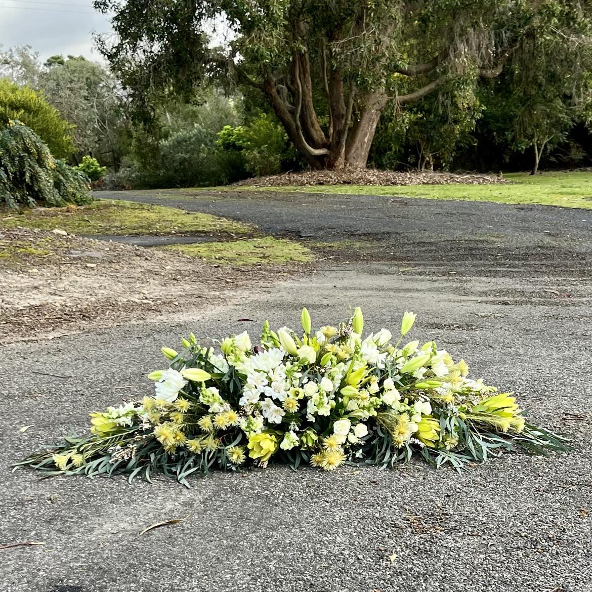 
                  
                    A floral funeral spray placed on a roadside, consisting of a sheaf of multicolored flowers including yellow and white, arranged to resemble a bouquet.
                  
                
