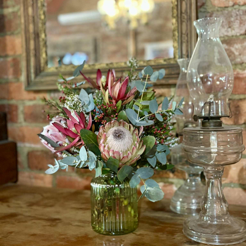 Floral arrangement in a vase on a table with a brick wall and mirror in the background