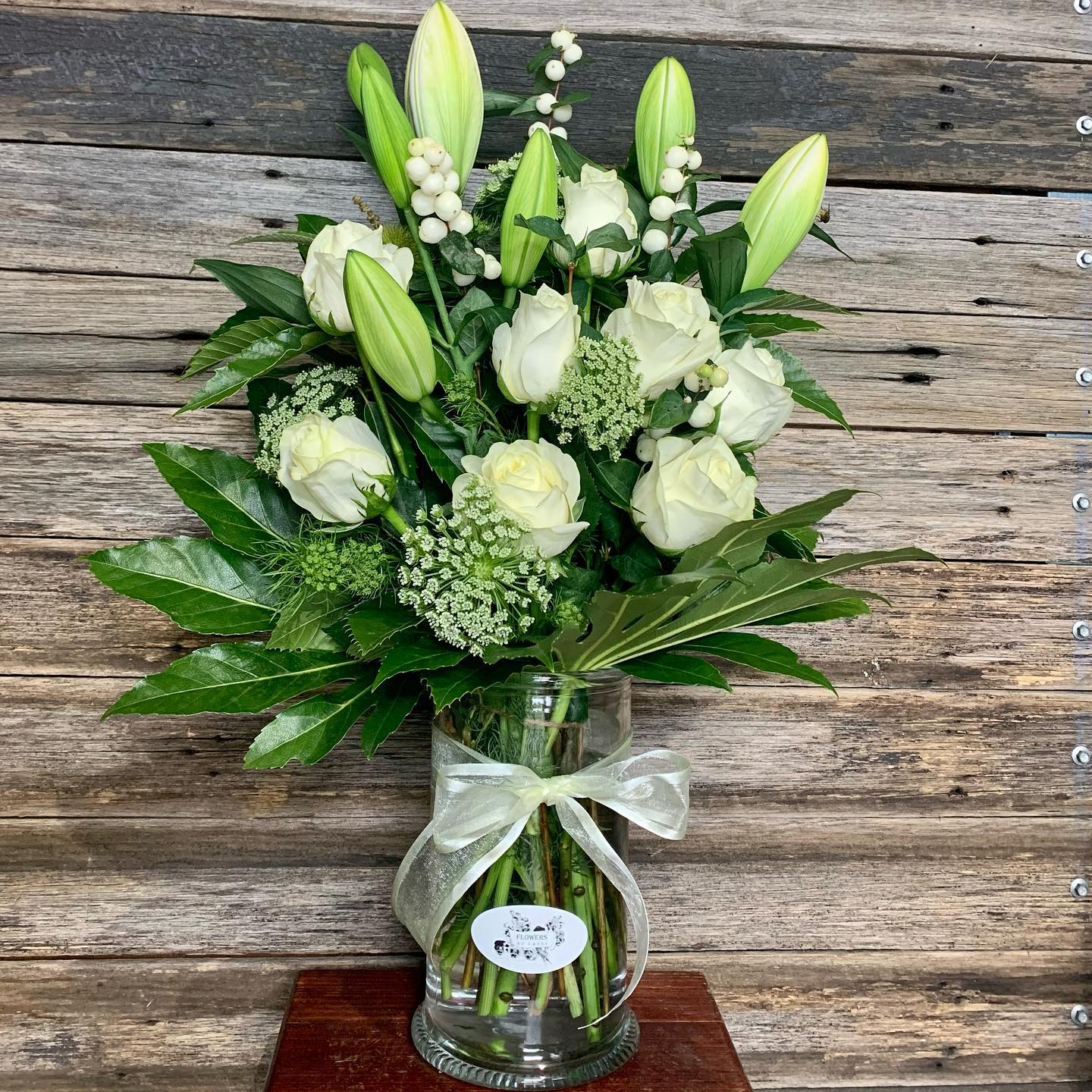 
                  
                    Bouquet of white flowers in a clear vase with a green ribbon 
                  
                